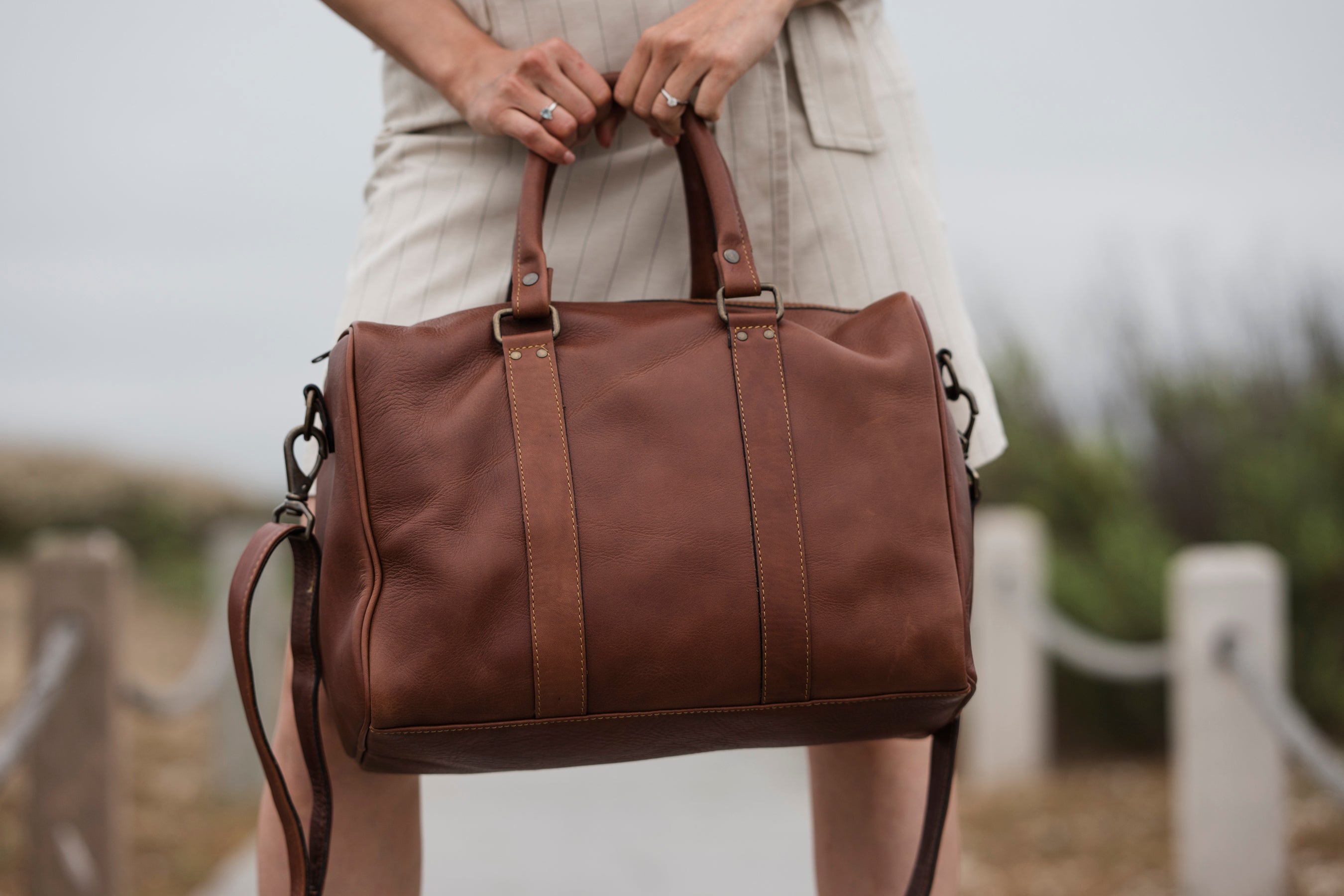 Brown leather duffel bag held by a person outdoors