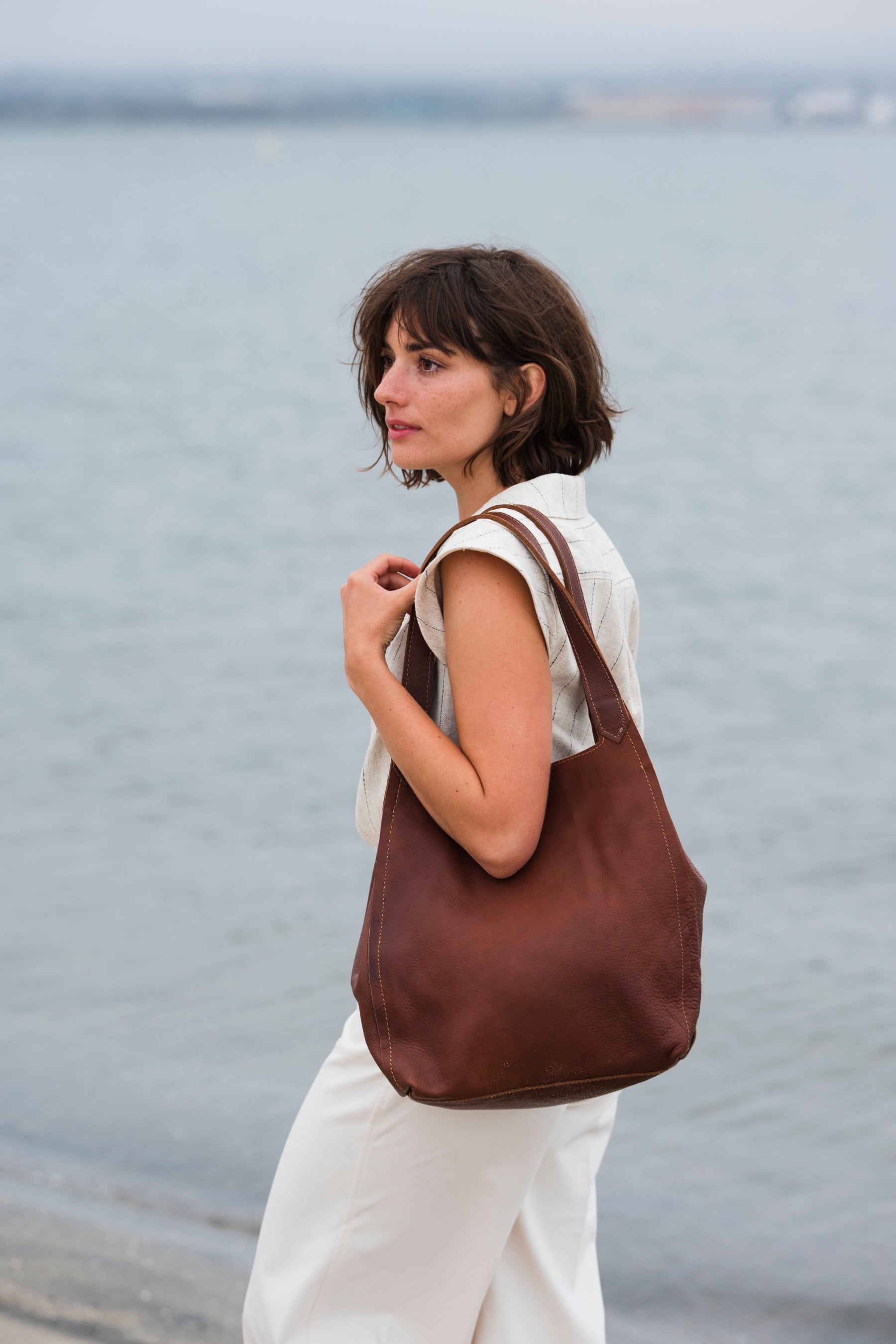 Woman holding an elegant leather brown leather bag by the ocean
