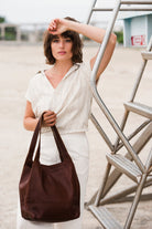 Woman holding a leather brown bag outdoors with a resort in the background